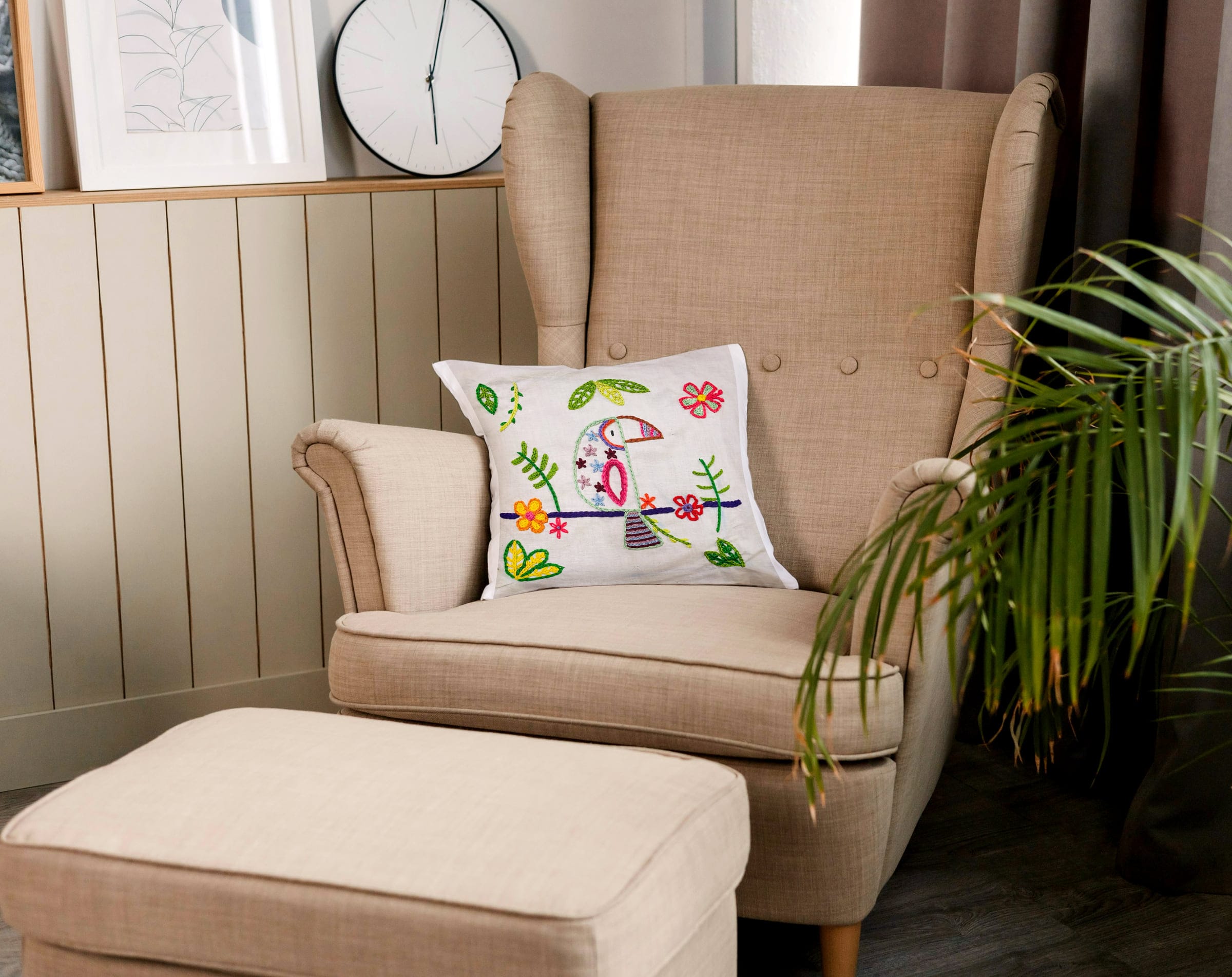 Embroidered toucan cushion styled on a beige armchair beside a plant