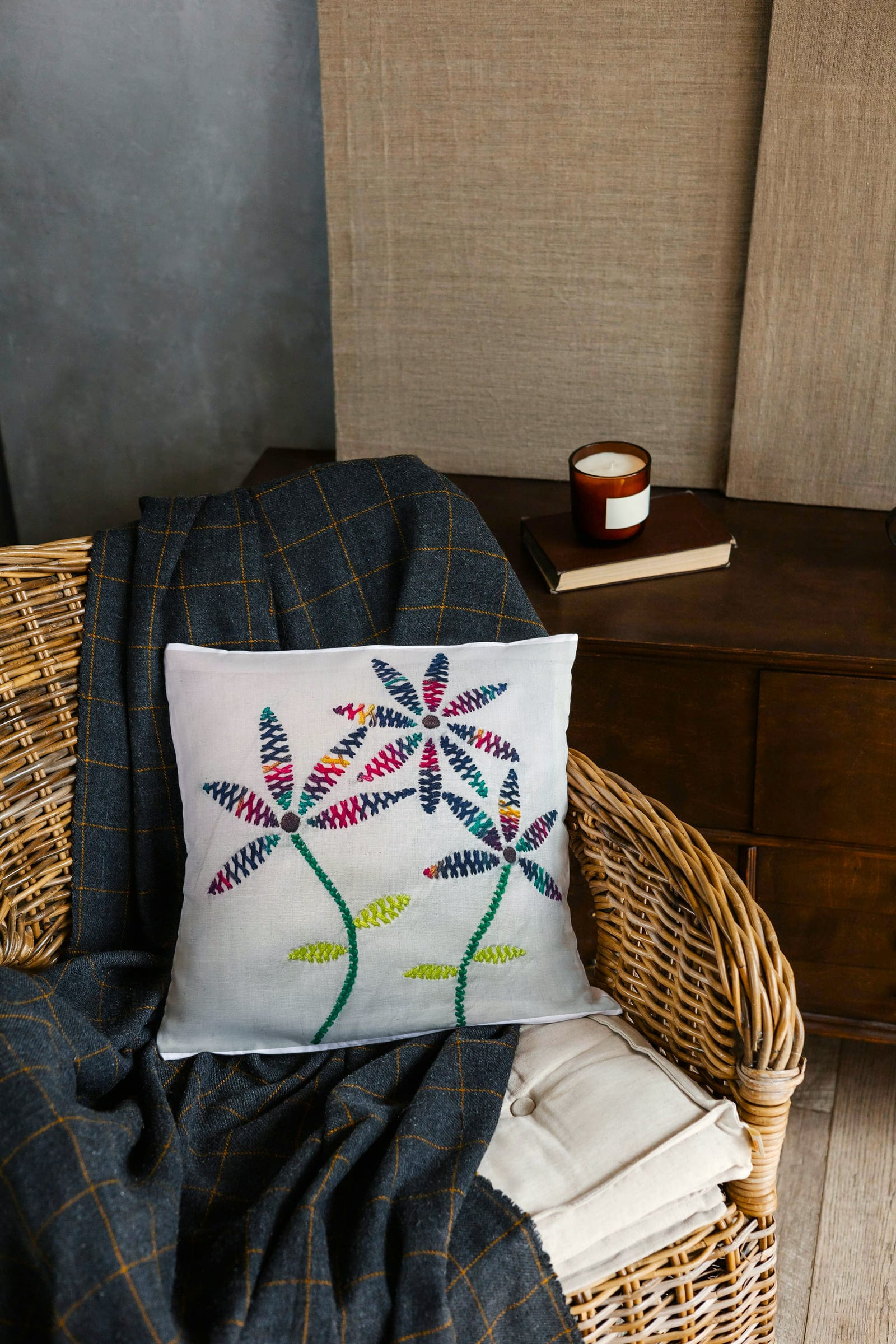 Flower-embroidered cushion on a woven armchair with a throw