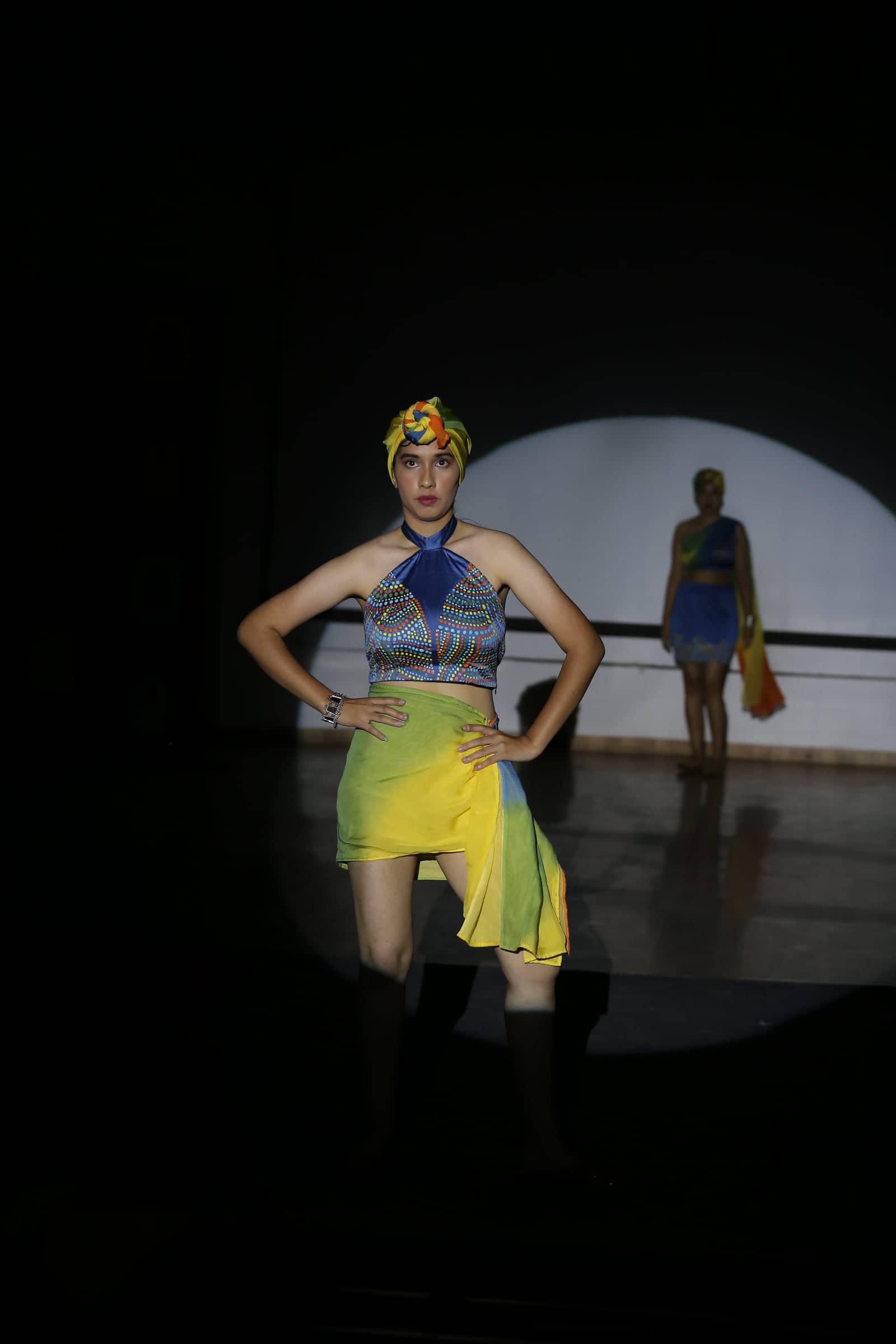 Model in a halter top and asymmetric skirt under a single spotlight